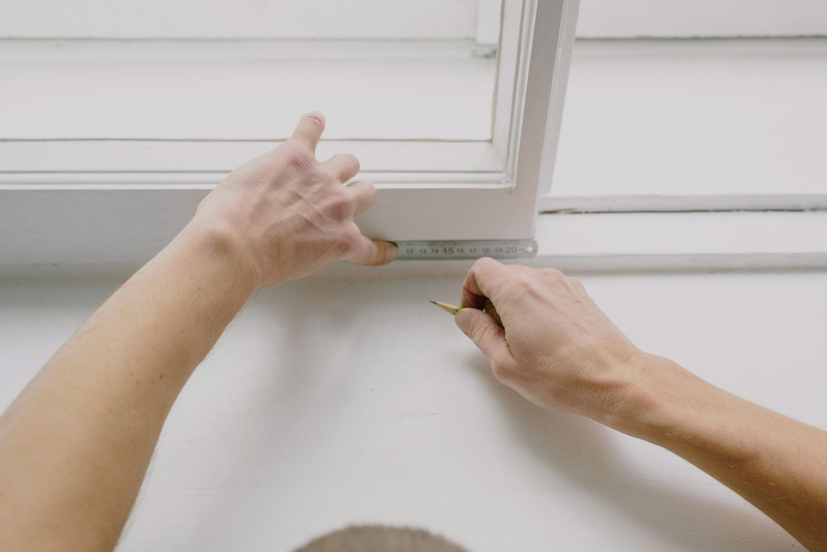 Hands measuring a white window frame
